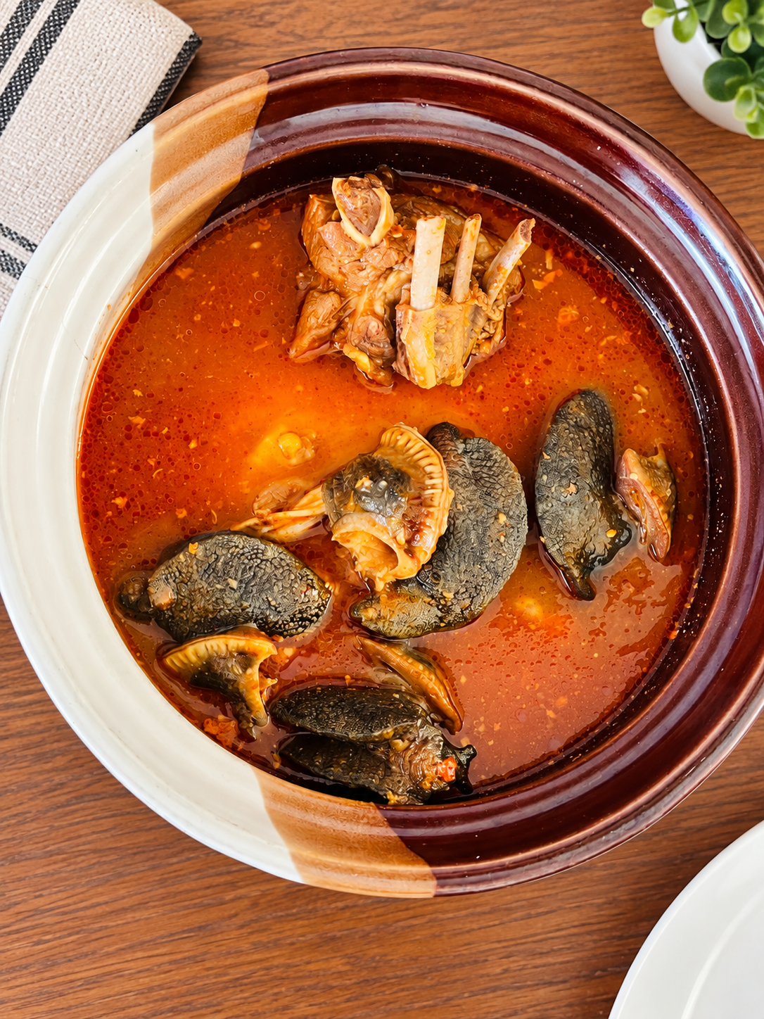 Earthenware bowl of peppery Ghanaian light soup with meat and snail