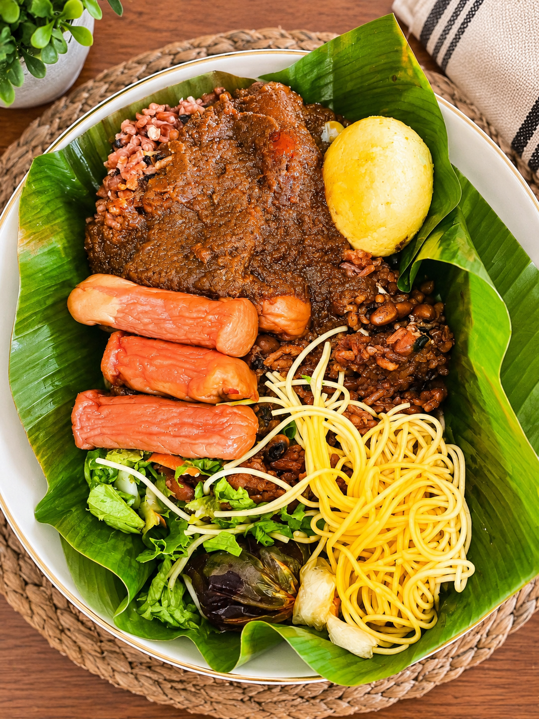 Bowl of waakye on banana leaf with spaghetti, boiled egg, salad and sausage